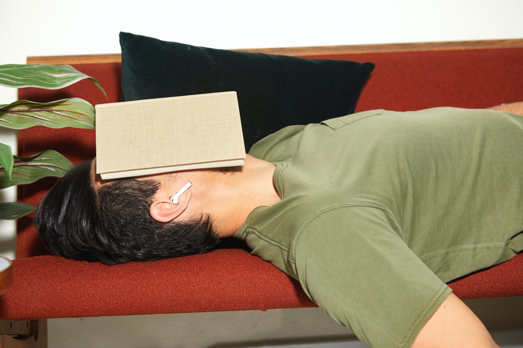 Man on couch with off white book covering face + aripods