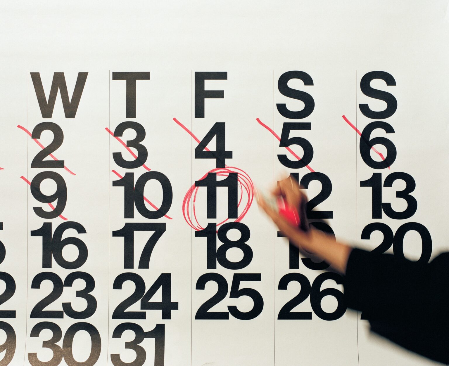 Hand circling numbers on calendar in red pen